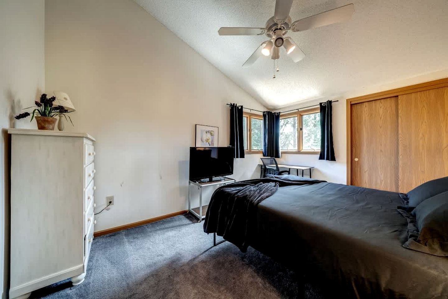 A bedroom with a bed, a desk with a computer, a television, a wardrobe, and a ceiling fan.