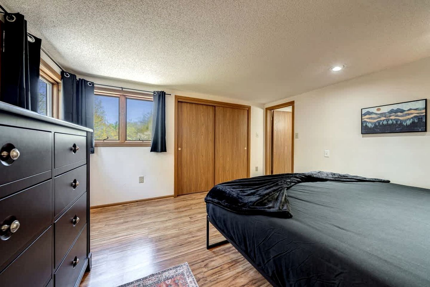 A bedroom with a bed, dresser, and a painting on the wall.