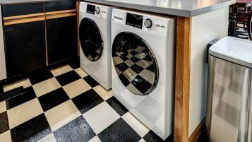 A laundry area with two front-loading washing machines, a sink, and a trash can.