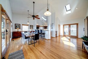 A spacious dining area with a high ceiling, wooden flooring, and a ceiling fan.