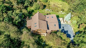 A large, multi-story house with a sloped roof, surrounded by dense greenery.