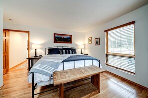 A bedroom with a bed, bedside tables, a bench, a window with blinds, and a door.