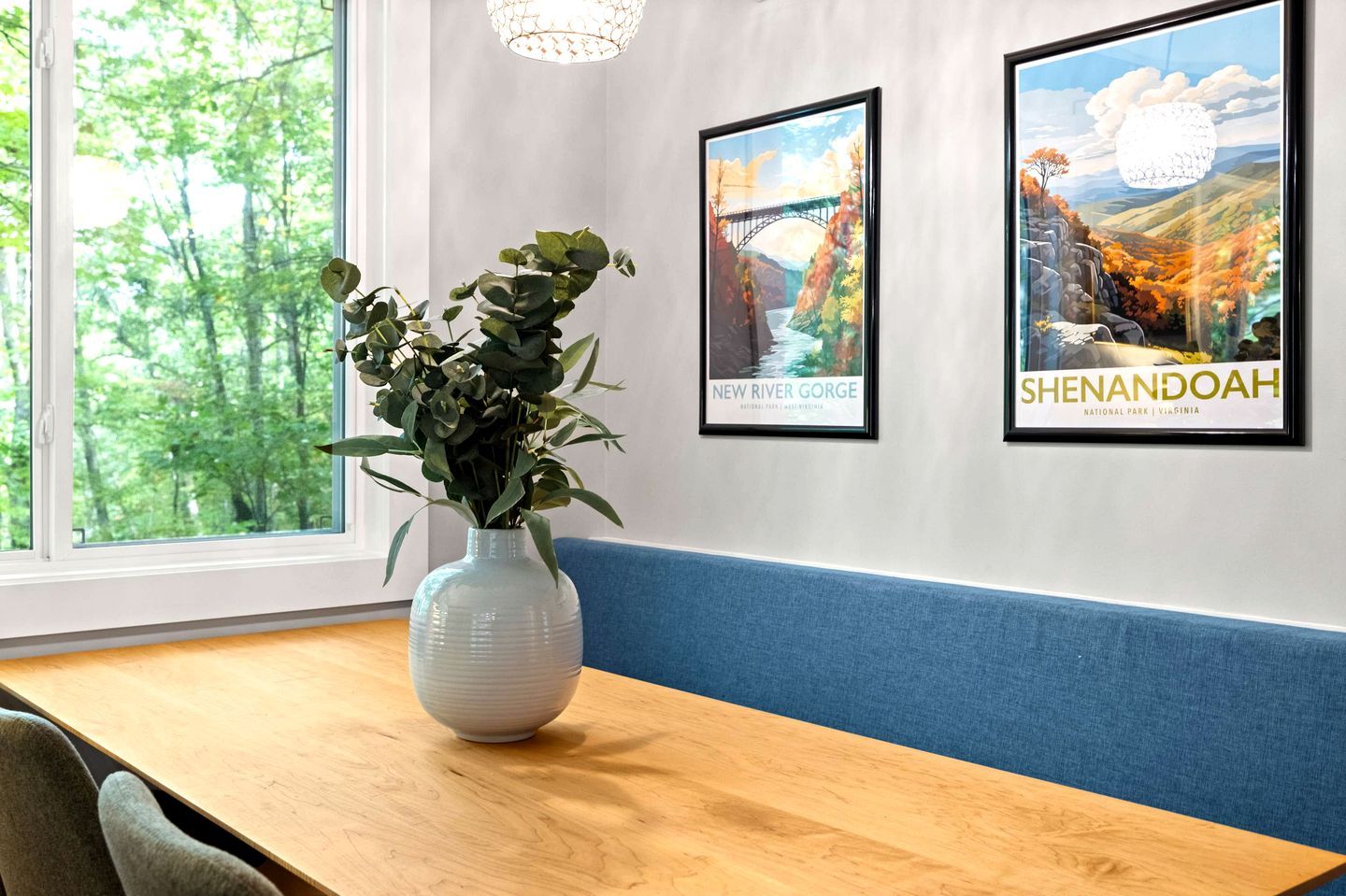 A room with a wooden table, a white vase with green plants, and two framed pictures on the wall.