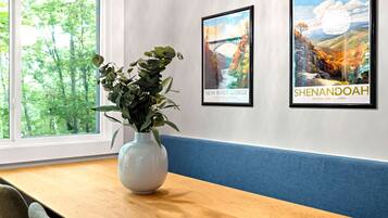 A room with a wooden table, a white vase with green plants, and two framed pictures on the wall.
