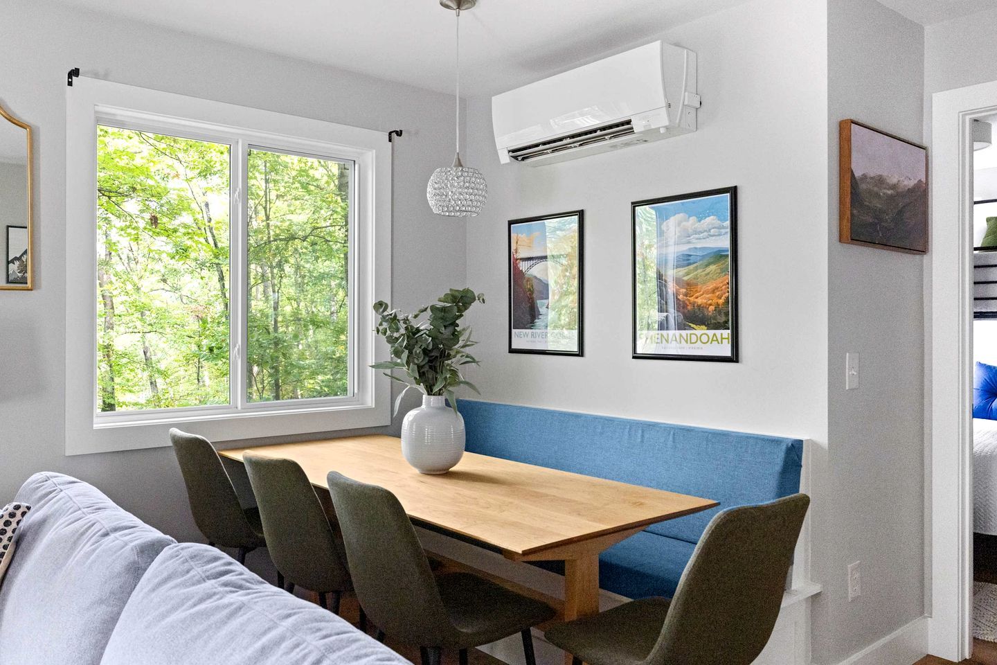 A dining area with a wooden table, chairs, a vase with plants, and framed pictures on the wall.