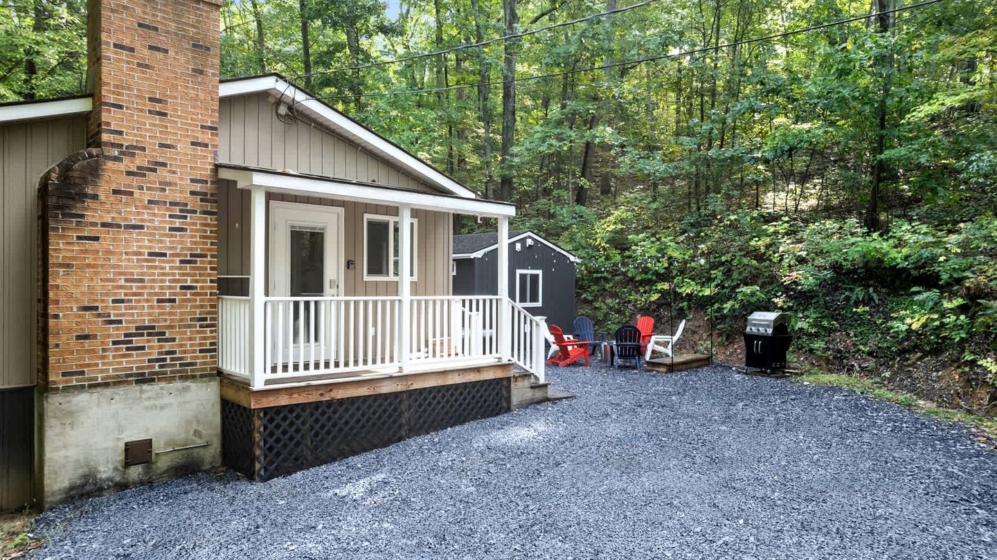 A cabin with a porch, outdoor seating, and a grill area.