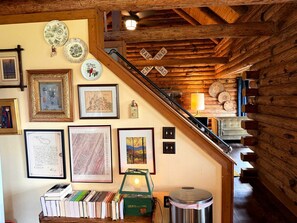 A staircase with wooden railings leading to a lower level, surrounded by framed pictures and books on the walls.