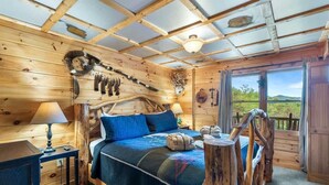 Ein Schlafzimmer einer Holzhütte mit einem Bett, einem Schreibtisch und einem Fenster mit Blick ins Freie.