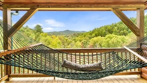 Una hamaca en una terraza de madera con vistas a un bosque y montañas.