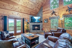 A cozy cabin interior with a stone fireplace, leather furniture, and a large TV screen. - Mountain View Cabin w/ Hot Tub & Game Room (Mineral Bluff)
