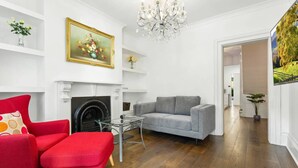 A living room with a fireplace, a red armchair, a grey sofa, and a chandelier.