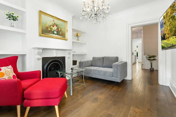 Una sala de estar con chimenea, un sillón rojo, un sofá gris y una araña.