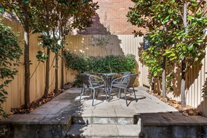 A patio with a table and chairs, surrounded by a wooden fence and trees. - Traditional 2-bed Terrace House in Millers Point (Sydney)