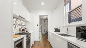 A modern kitchen with white cabinetry, a marble backsplash, a gas stove, a dishwasher, and a view into the dining area.