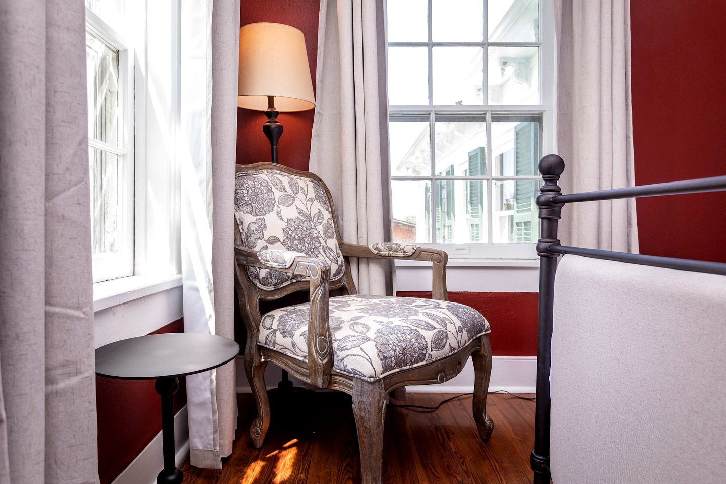 Une pièce avec une chaise en bois, une petite table, une lampe et une fenêtre avec des rideaux.