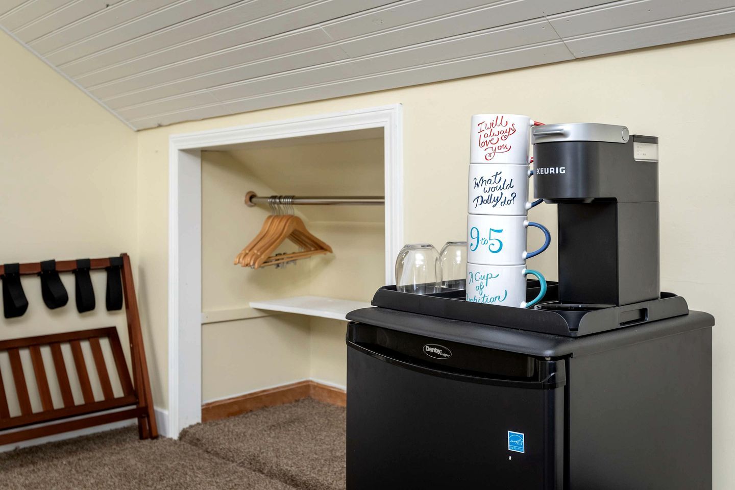A kitchenette with a Keurig coffee maker, a refrigerator, and a small shelf with a mug.