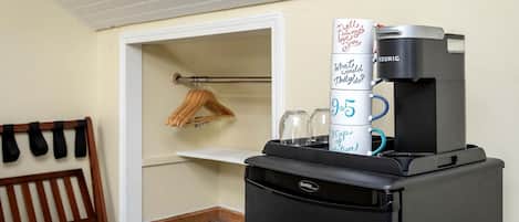 Une petite cuisine équipée d’une machine à café Keurig, d’un réfrigérateur et d’une petite étagère sur laquelle se trouve une tasse.