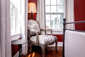 Une pièce avec une chaise en bois, une petite table, une lampe et une fenêtre avec des rideaux.