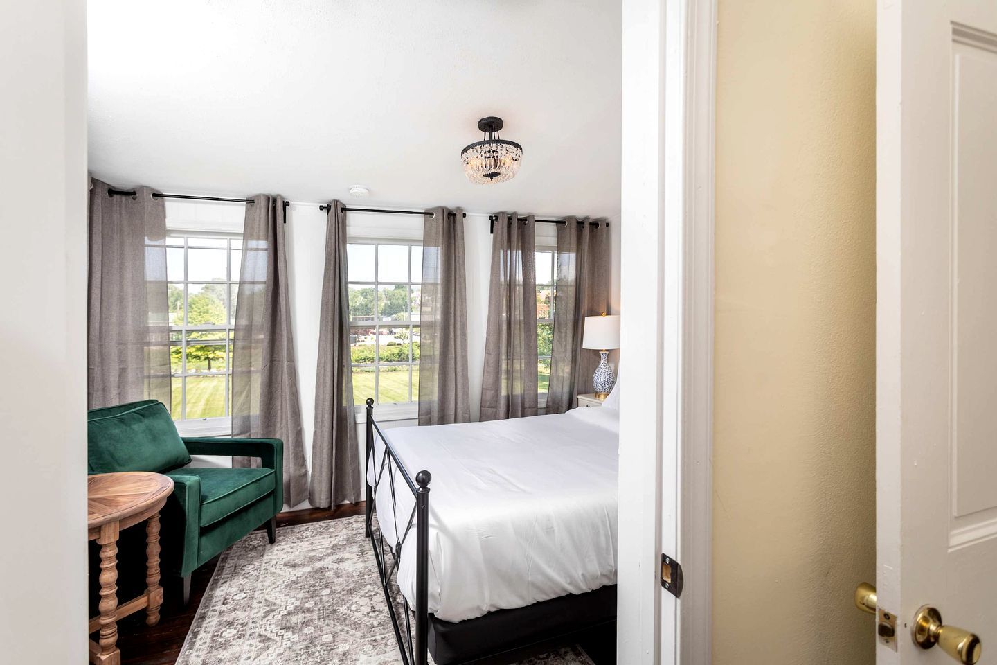 A hotel room with a bed, a green chair, a small table, and a view of the outdoors.