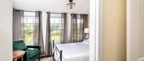 Una habitación de hotel con una cama, una silla verde, una mesita y vistas al exterior.