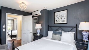 A bedroom with a bed, bedside lamps, a nightstand, a dresser, a chandelier, an air conditioning unit, a door to another room, and a framed artwork on the wall. - Romantic Mountain Vacation Rentals with Garden Views near Shenandoah National Park Virginia (Luray)