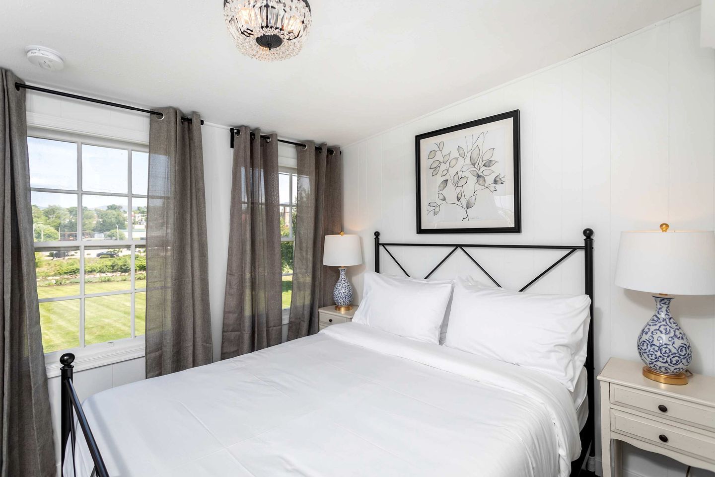 A neatly arranged bedroom with a bed, two bedside tables with lamps, a framed artwork on the wall, and a window with curtains.