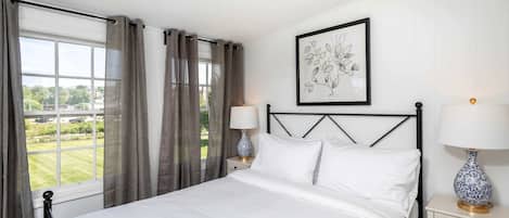 A neatly arranged bedroom with a bed, two bedside tables with lamps, a framed artwork on the wall, and a window with curtains.