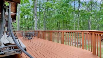 A wooden deck with a table and chairs, surrounded by a wooden railing, overlooking a forested area.