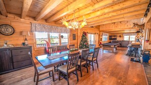 L'interno accogliente di un cottage con un tavolo da pranzo in legno, sedie, un albero di Natale e un tavolo da biliardo.