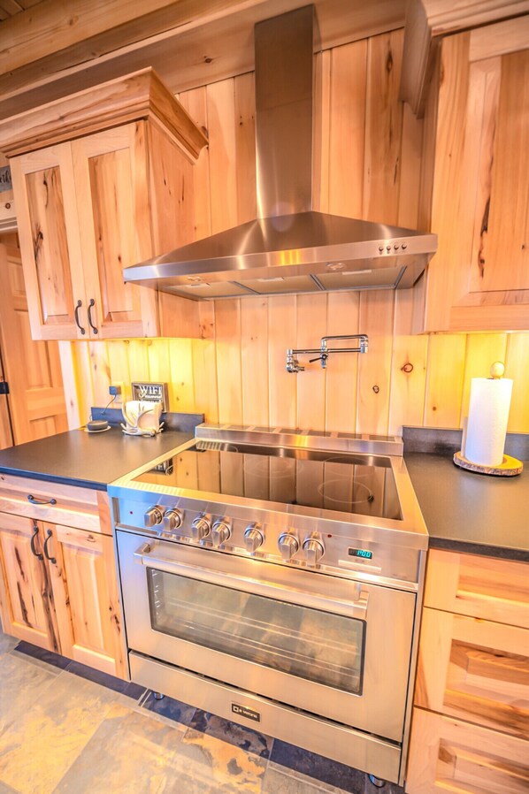 A kitchen with wooden cabinets, a stainless steel range hood, a double oven, and a countertop with a WiFi router and a paper towel holder.