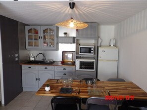 A compact kitchen with grey cabinets, a wooden dining table, and a hanging light fixture.