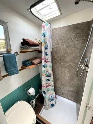 Ein kleines Badezimmer mit Dusche, Toilette und einem Ablagebereich mit Handtüchern.