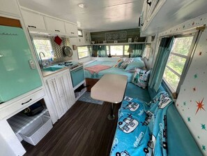 Interior compacto de una caravana con kitchenette, dos zonas para dormir y una mesa de comedor.