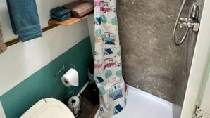 A compact bathroom with a shower, toilet, and a small shelf with towels.