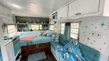 Une chambre compacte dans un camping-car, comprenant un lit, une petite kitchenette et une fenêtre avec des rideaux.