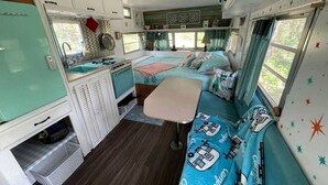 A compact RV interior with a kitchenette, two sleeping areas, and a dining table.