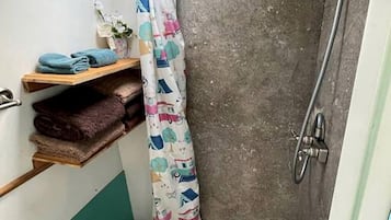 A small bathroom with a shower, a toilet, a shelf with towels, and a skylight.