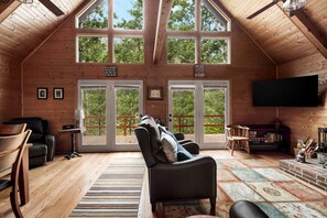 A cozy cabin interior with a large window, a fireplace, and a television.