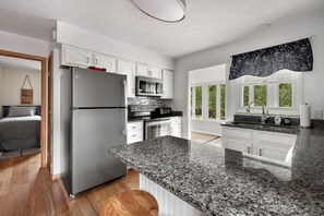 A modern kitchen with white cabinetry, a granite countertop, stainless steel appliances, and a view of greenery outside.