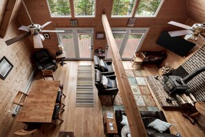 A cabin with a wooden interior, a dining area, a seating area with a fireplace, and a ceiling fan.
