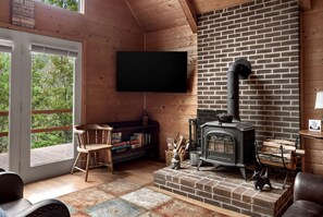 A cozy cabin interior with a fireplace, a bookshelf, a television, and a large window.