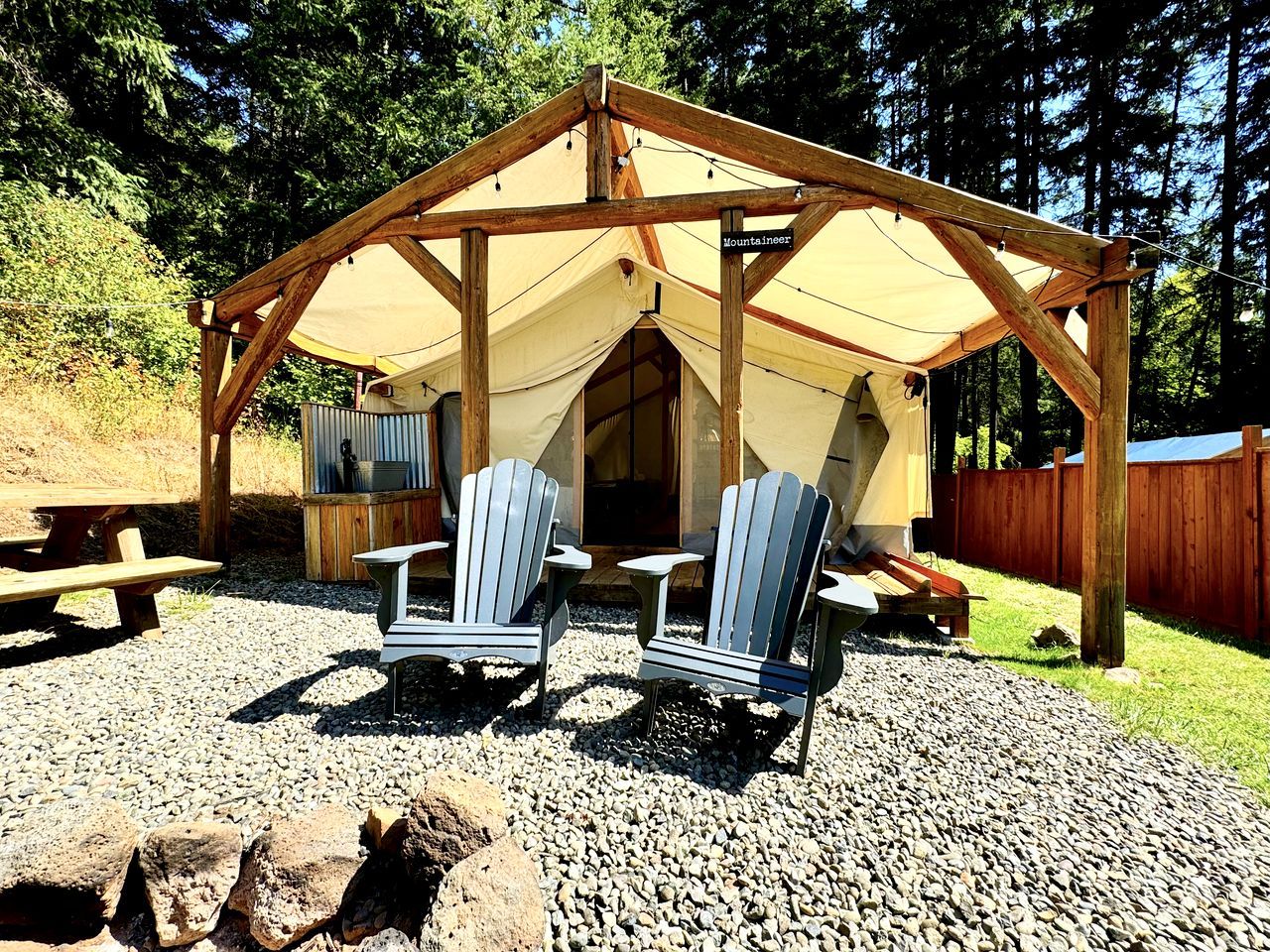 En paviljong av trä med ett tält, två Adirondack-stolar och ett picknickbord.