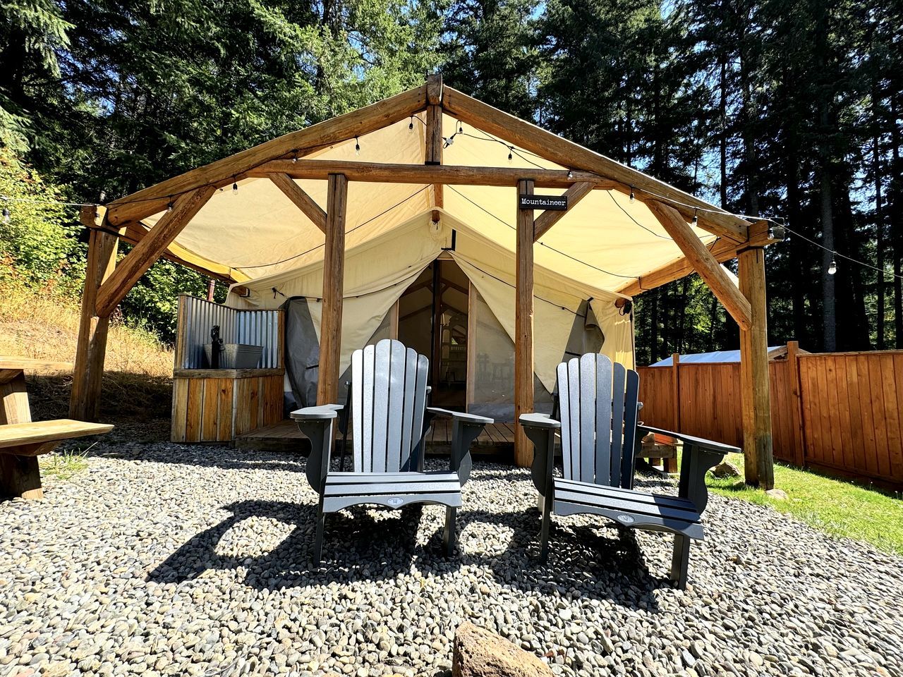 A wooden gazebo with a tent, two Adirondack chairs, and a grill.