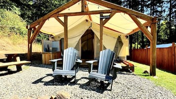 A wooden pavilion with a tent, two Adirondack chairs, and a picnic table.