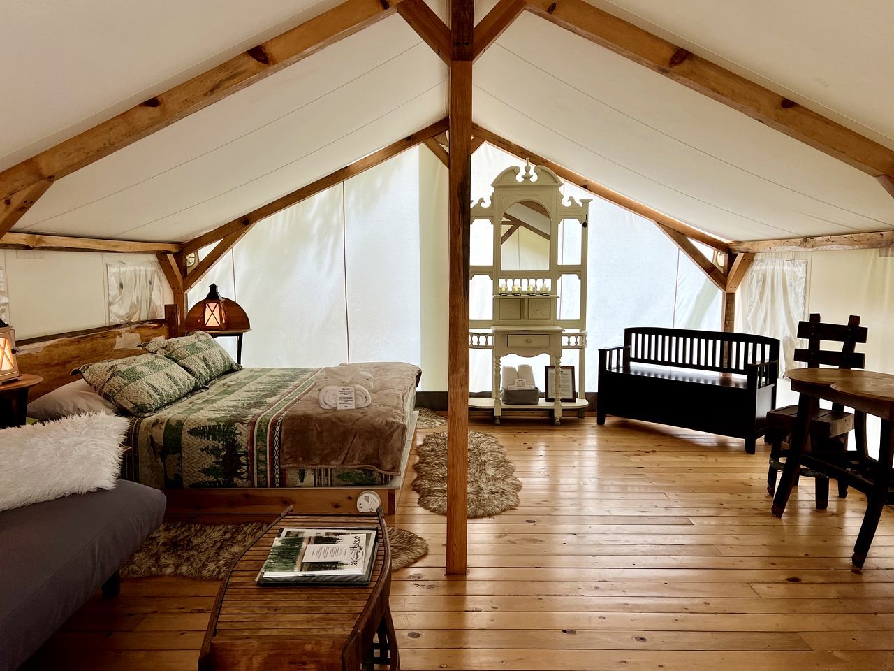 A tented accommodation with a bed, a table, a bench, and a small table with a lamp.