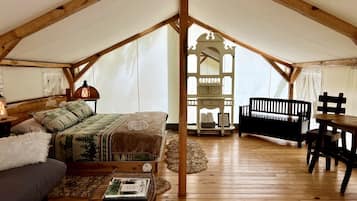 A tented accommodation with a bed, a table, a bench, and a small table with a lamp.
