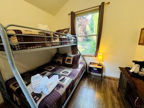 A bunk bed room with a window, a bedside table, and a lamp.