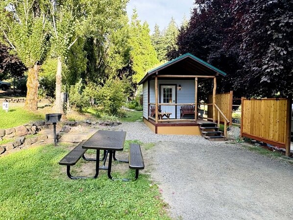 A small cabin with a porch, a picnic table, and a wooden fence.