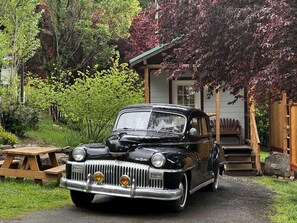 Un coche negro antiguo estacionado frente a una casa con un porche de madera y una mesa de picnic.