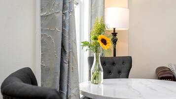 A room with a round marble table, a vase with flowers, a lamp, and a tufted chair.